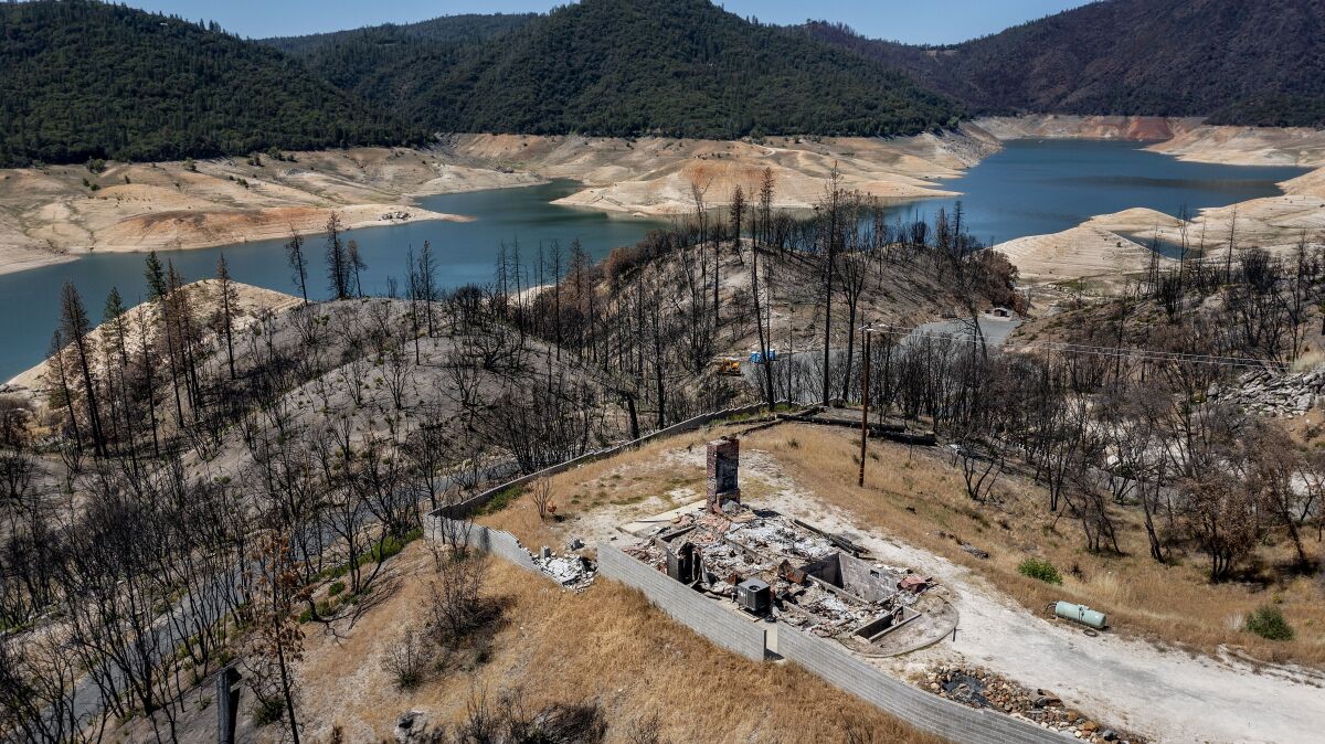 A burned home and trees next to a reservoir with low water levels