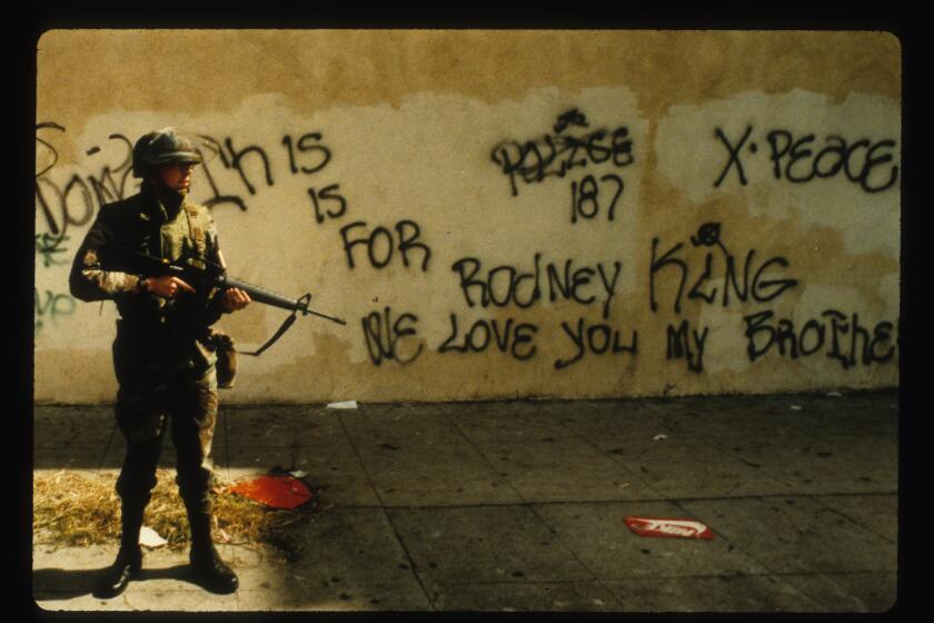 4–30–1992 National Guardsmean stands at alert near graffiti that spells out support for Rodney King.