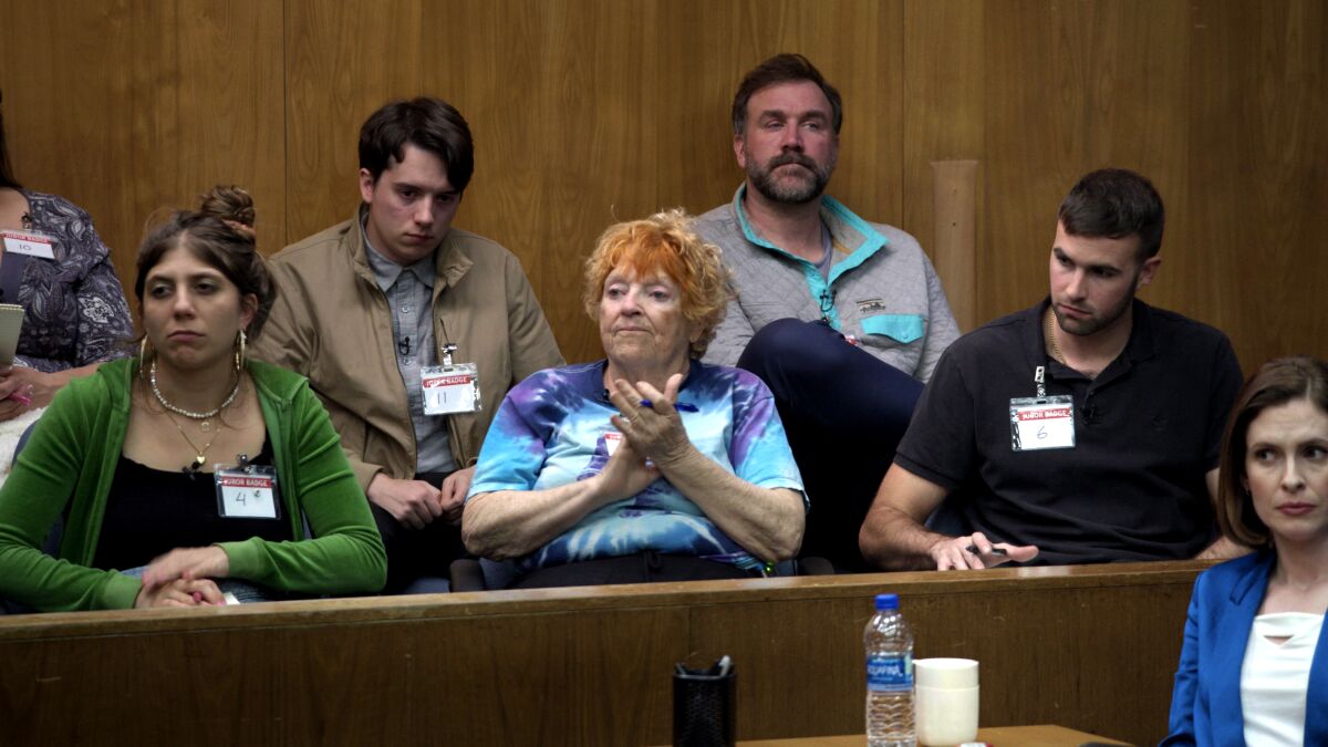 Five people sit in a jury box in a courtroom.