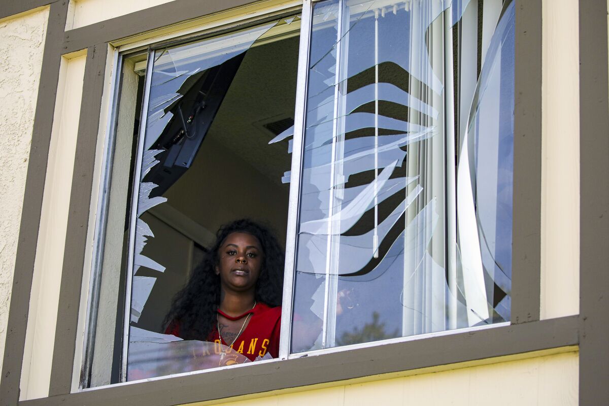 A woman looks out a broken window.