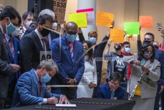 Gov. Brian Kemp, lower left, signs HB 426, hate-crimes legislation, into law as demonstrators hold signs asking him to veto HB 838 in the North Wing of the Georgia State Capitol building Friday, June 26, 2020. Kemp signed into law House Bill 426 which would impose additional penalties for crimes motivated by the victim’s race, color, religion, national origin, sexual orientation, gender or disability. (Alyssa Pointer/Atlanta Journal-Constitution via AP)