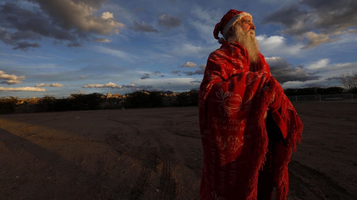 James Zyla, 68, stands in the late afternoon light wrapped in a red blanket across from where he is staying at the Ramada hotel in Kingman, Ariz. For years, the white-bearded man in the Santa Claus outfit has been a familiar sight around this isolated high desert town.