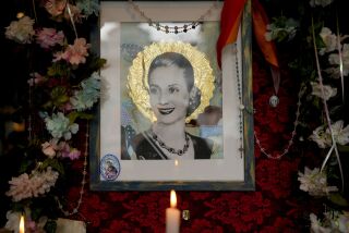 A candle stands near a picture of Argentina's late former first lady Maria Eva Duarte de Peron, better known as "Evita" at "El Santa Evita" restaurant in Buenos Aires, Argentina, Sunday, July 24, 2022. Argentines commemorate the 70th anniversary of the death of their most famous first lady on Tuesday, Evita who died of cancer on July 26, 1952, at the age of 33. (AP Photo/Natacha Pisarenko)