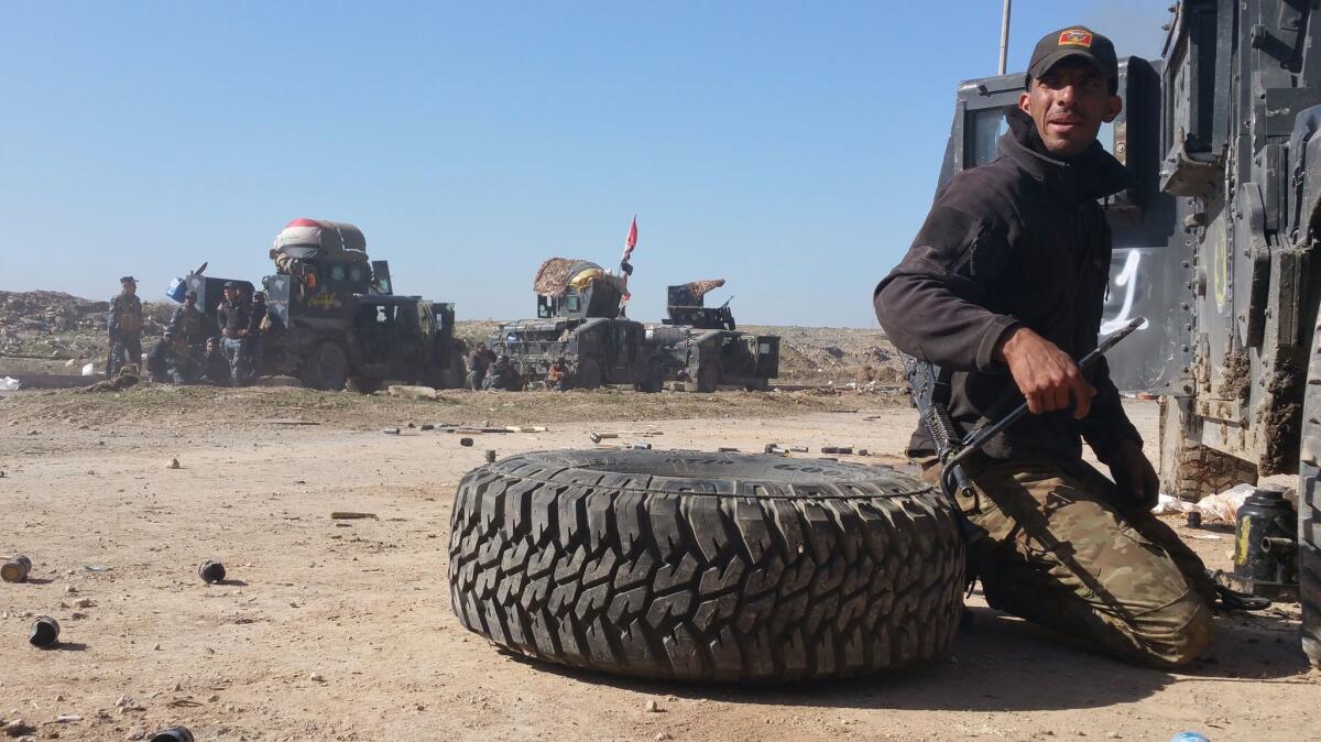A counter-terrorism service soldier changes a Humvee tire under fire near west Mosul.