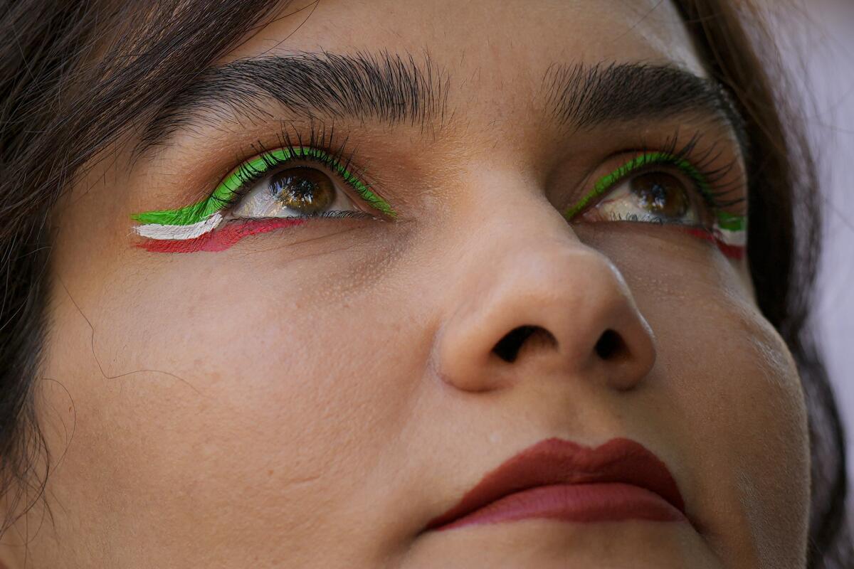 A woman, wearing eyeliner in green, white and red, looks up 