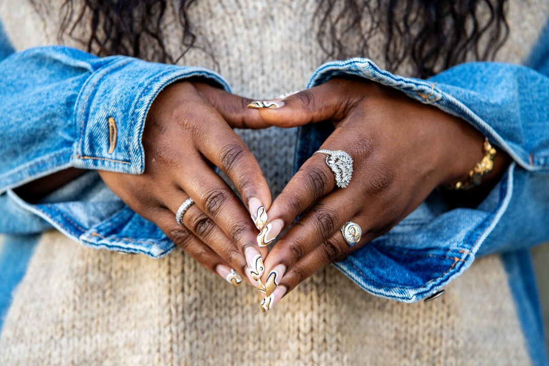 The hands of a woman, fingertips joined, decorated with different rings and peeking out from the sleeves of jeans.