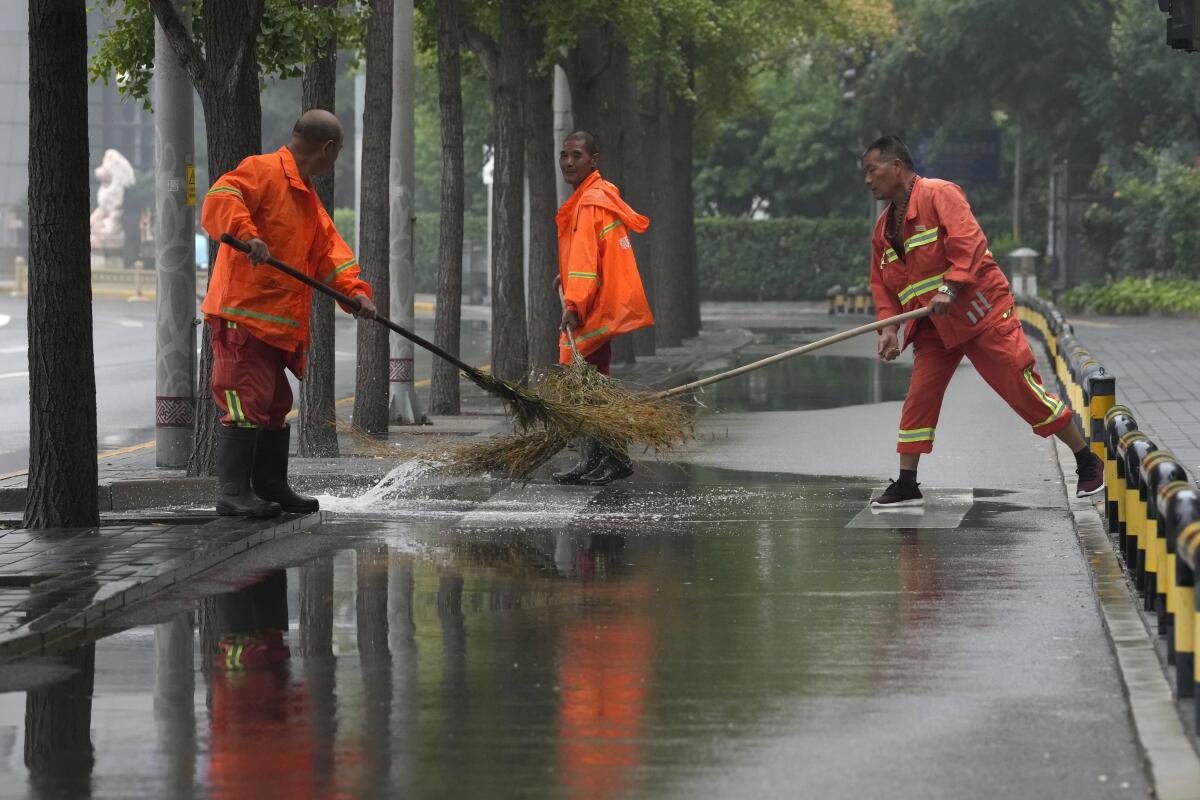 Workers clear a puddle of water after a rainstorm in Beijing, Sunday, Aug. 14, 2022. (AP Photo/Ng Han Guan)
