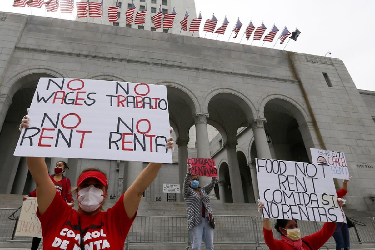 Masked demonstrators hold up signs on the steps of a building. One sign reads, No wages, no rent