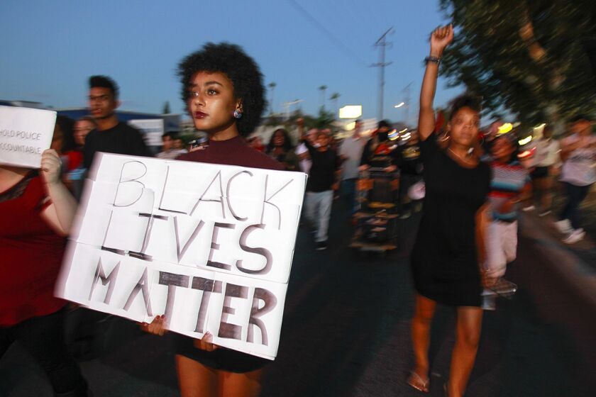 A woman carries a sign as she and a large crowd of people protesting the police shooting of a black man march down Broadway in El Cajon on Wednesday.