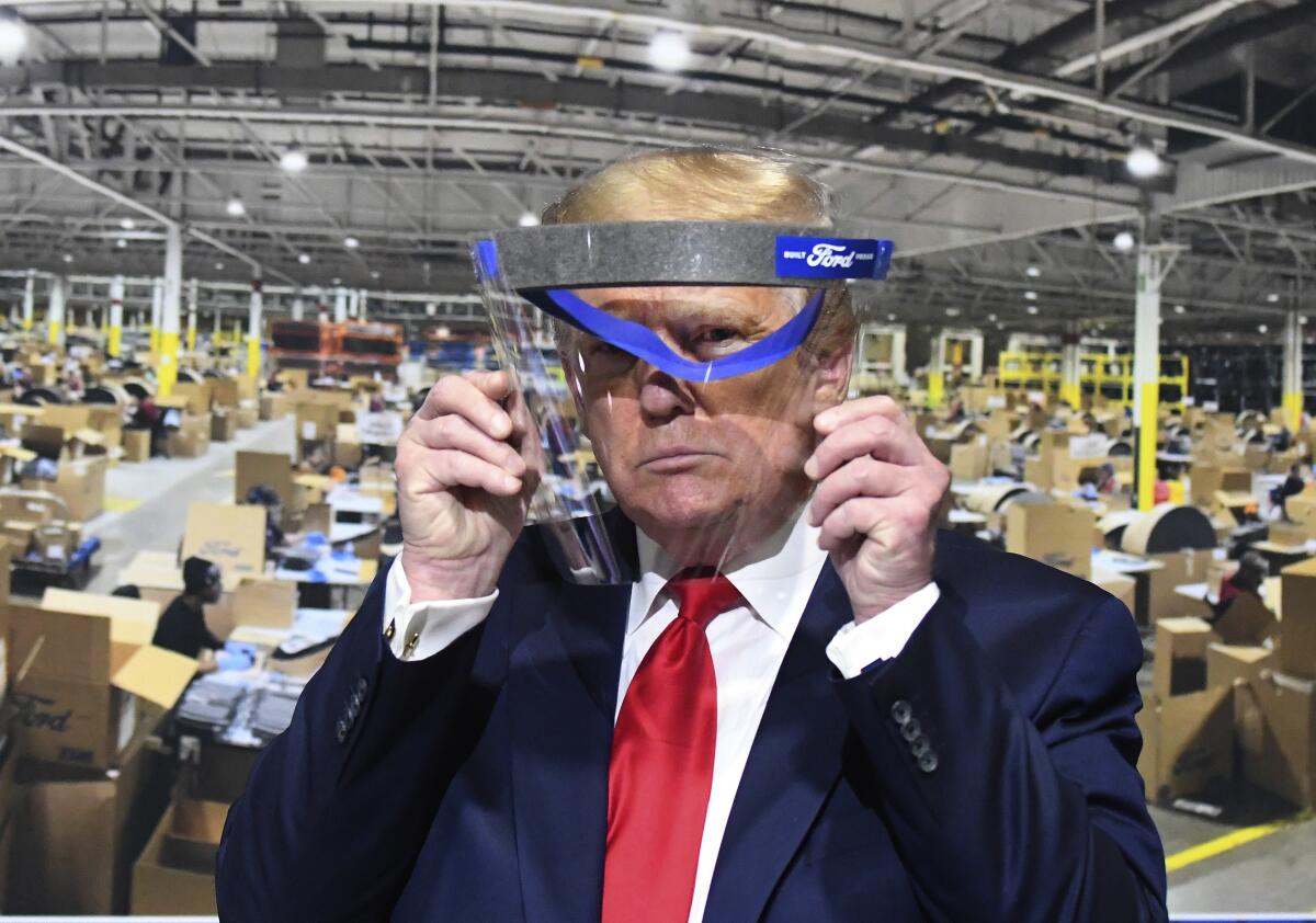 President Donald Trump looks through a face shield, in front of poster of the manufacturing of these shields, while touring Ford Motor Co.'s Rawsonville Components Plant in Ypsilanti, Michigan on Thursday, May 21, 2020.