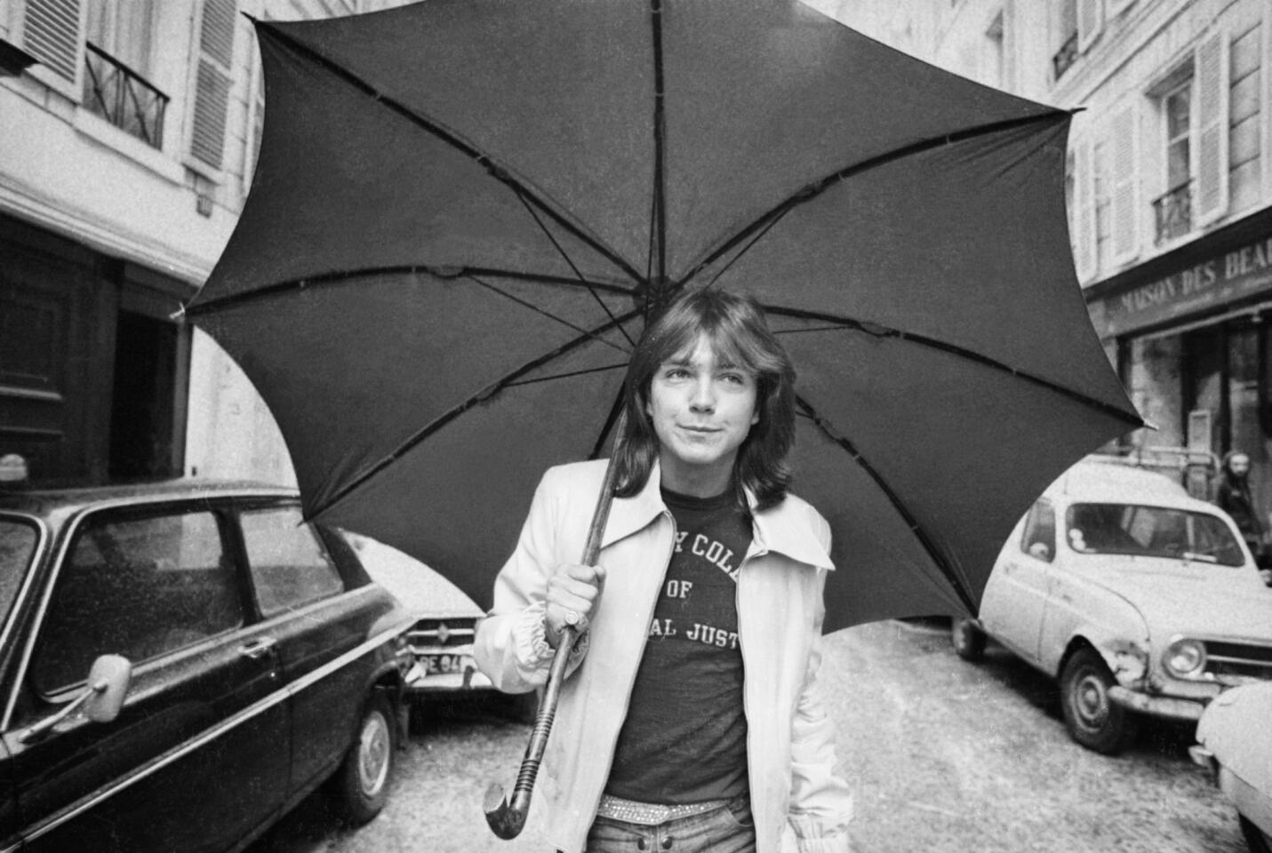 Clutching an umbrella, David Cassidy wanders down a road in London in 1974.
