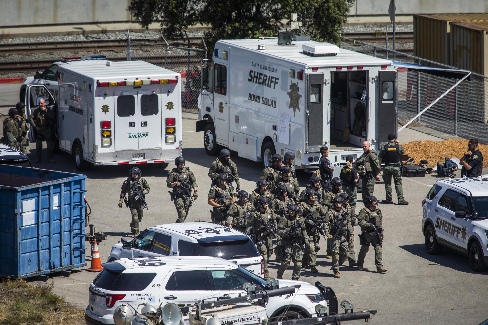 Many men in camouflage move through an area with several large vehicles.