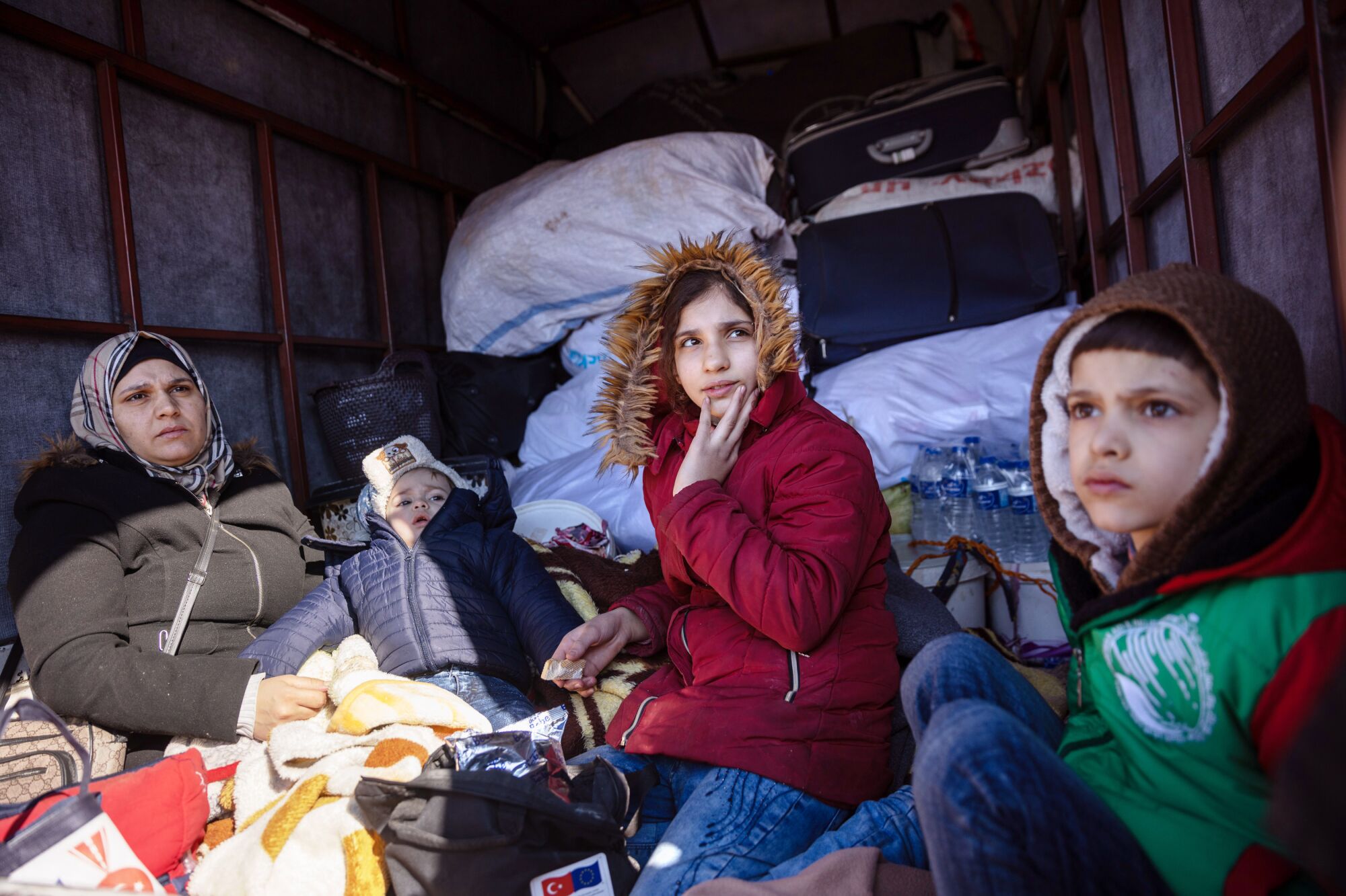 A woman sits in the back of a truck with several children, all wearing coats.