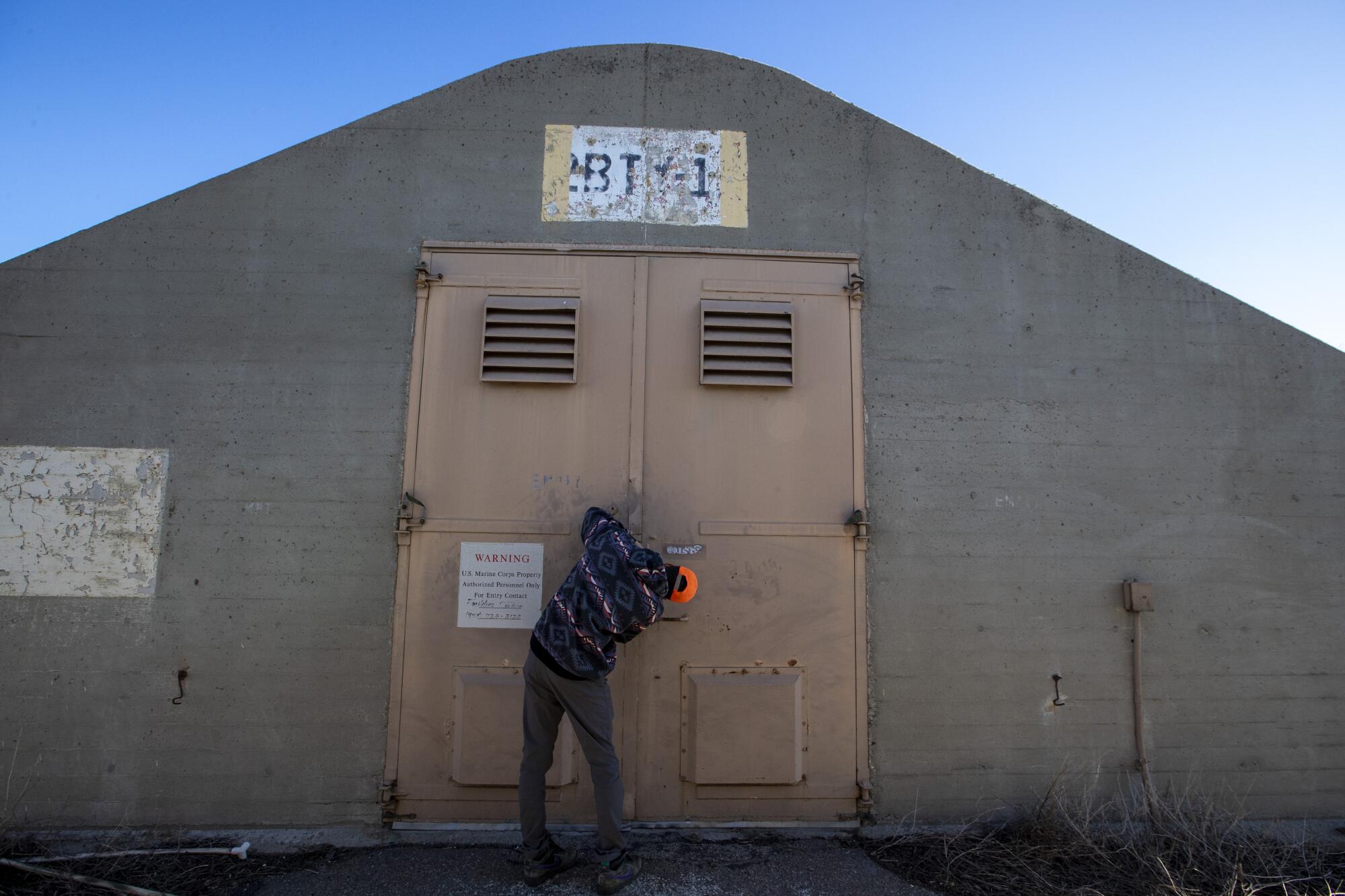 A man unlocks the doors of a concrete and steel WWII munitions bunker 