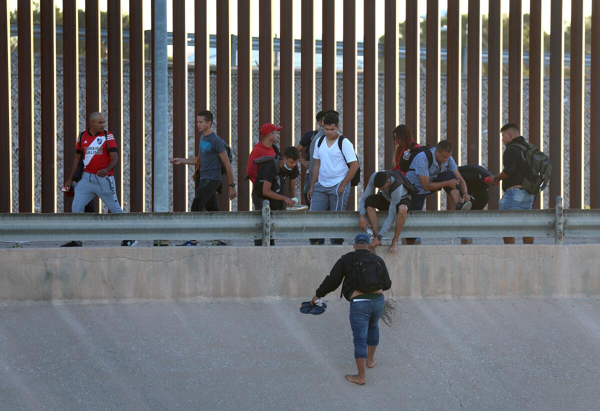 migrants along a tall border fence 