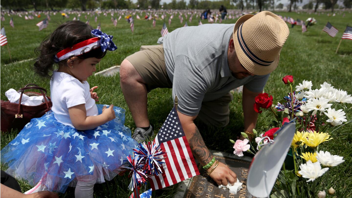 Luis Ruelas, 28, of Simi Valley, cleans the grave marker of Roy Kenneth de Bruin who served in the Air Force during the Vietnam War. At left is de Bruin's granddaughter Olivia Ruelas, 16-months old.