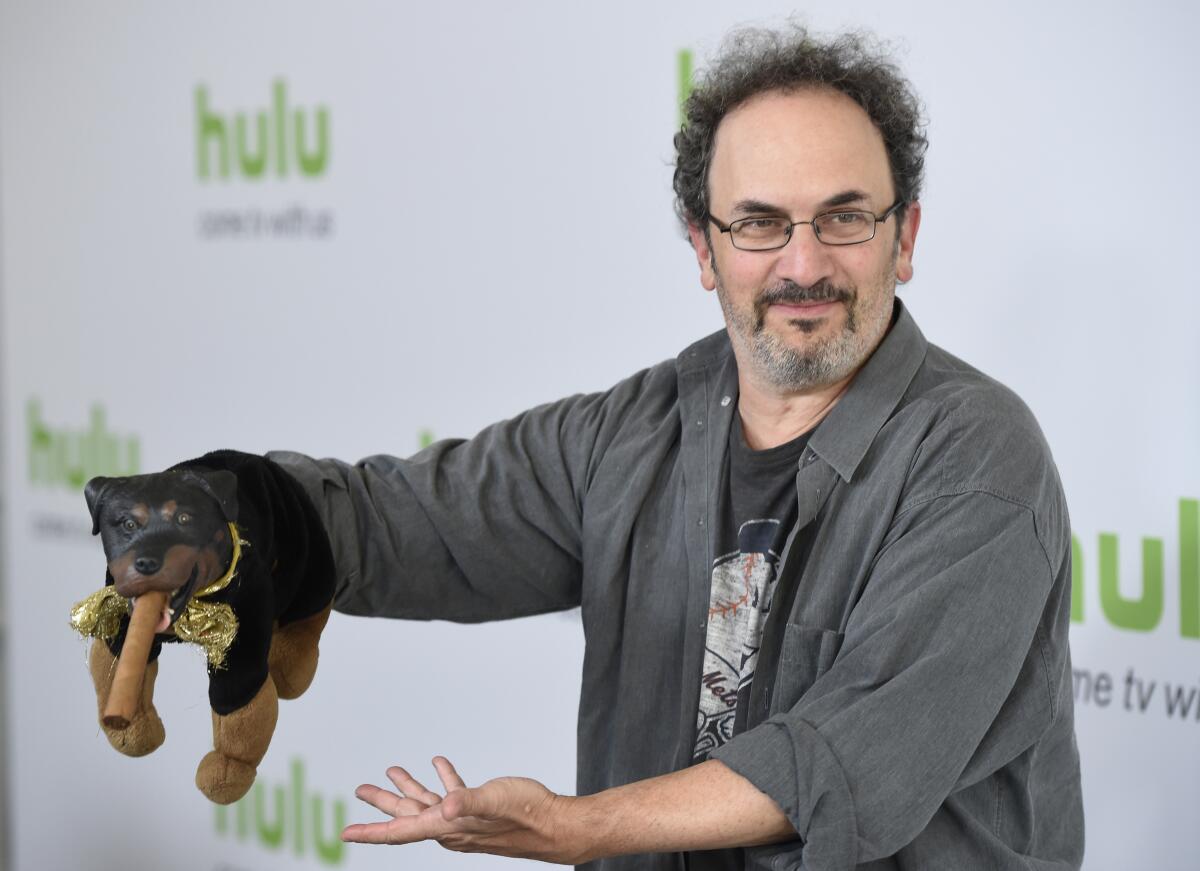 A man holds a puppet in front of a Hulu-branded step-and-repeat backdrop