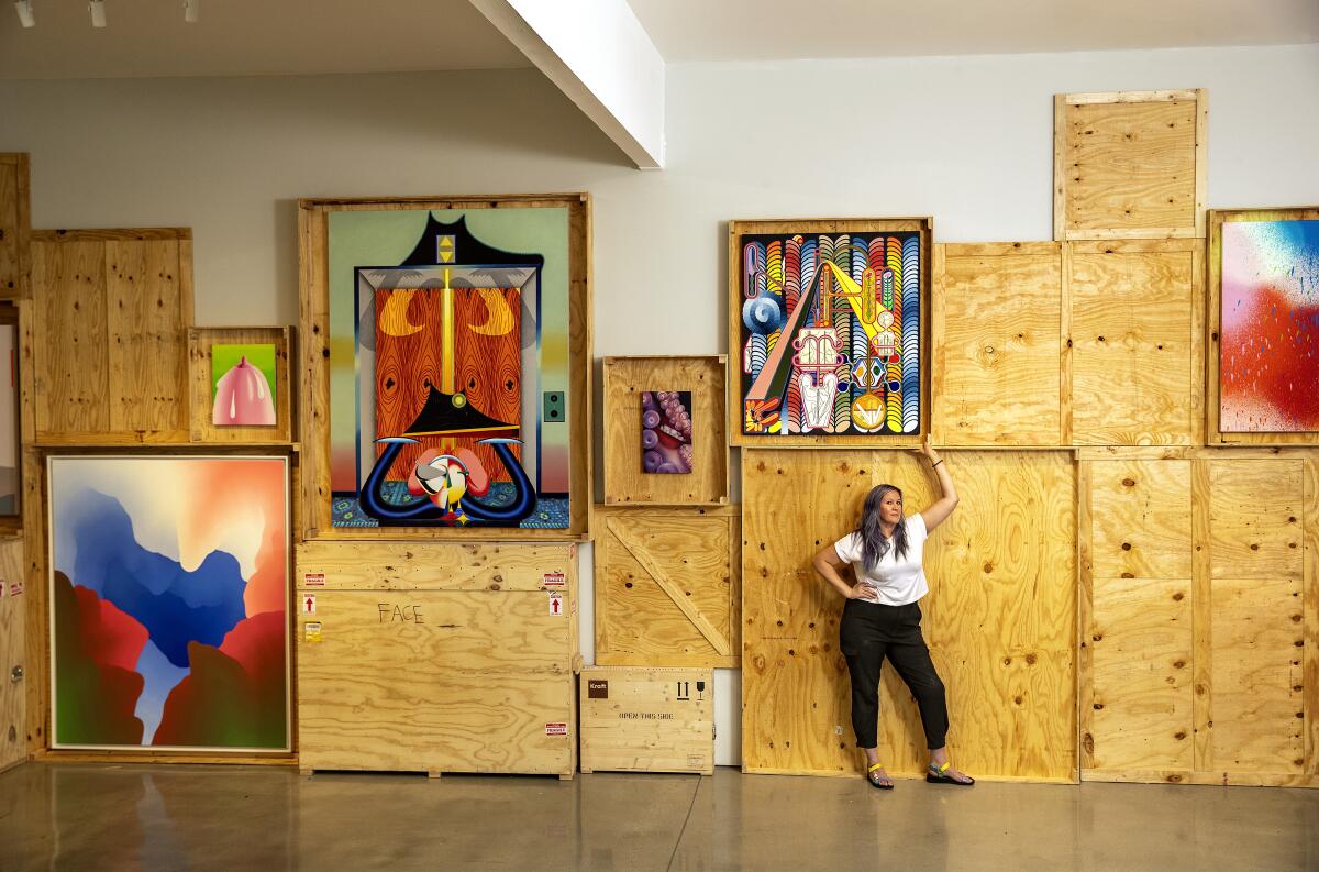 Kathy Grayson stands in front of colorful paintings and crates.