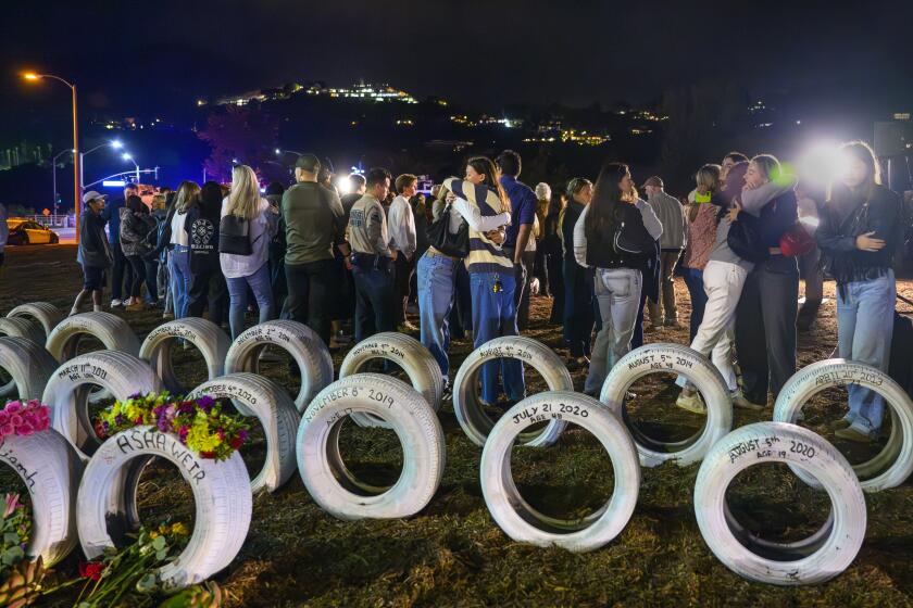 MALIBU, CA - OCTOBER 17, 2024: Former classmates and friends embrace during a candlelight vigil near the "Ghost Tire" memorial for the four Pepperdine students killed one year ago on Pacific Coast Highway October 17, 2024 in Malibu, California. Sixty one people have been killed along this stretch of Pacific Coast Highway.(Gina Ferazzi / Los Angeles Times)