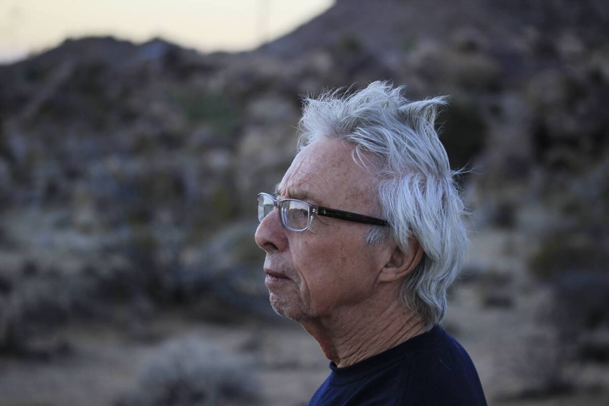 Harold Budd outdoors with a hill of foliage behind him.