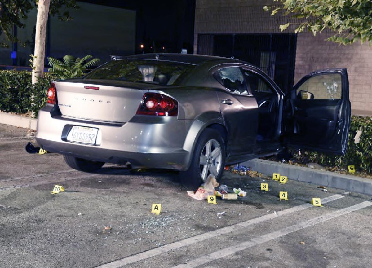 A crashed Dodge sedan with its passenger-side door open; broken glass and evidence markers on asphalt nearby