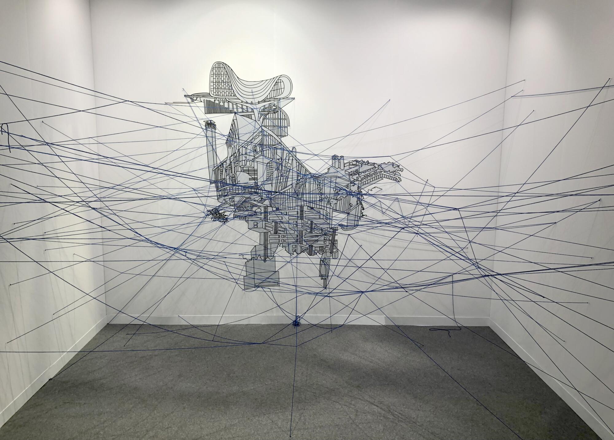 A wall drawing in a gallery booth features a mash-up of building architectures from which emerge a web of strings