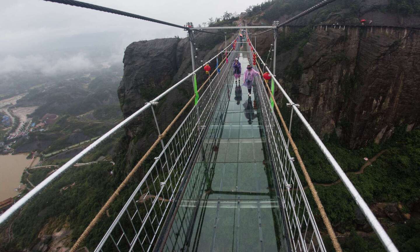 Chinese tourists walk across a glass-bottomed suspension bridge in the Shinuizhai mountains in Pingjang county, Hunan province some 150 kilometers from Changsha on October 7, 2015. The bridge, originally a wooden walkway spanning some 300 meters across the 180-meter deep valley, reopened two weeks ago following renovations as a glass-bottomed tourist attraction.