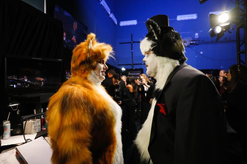 Two adults dressed in large cat suits backstage at an awards show