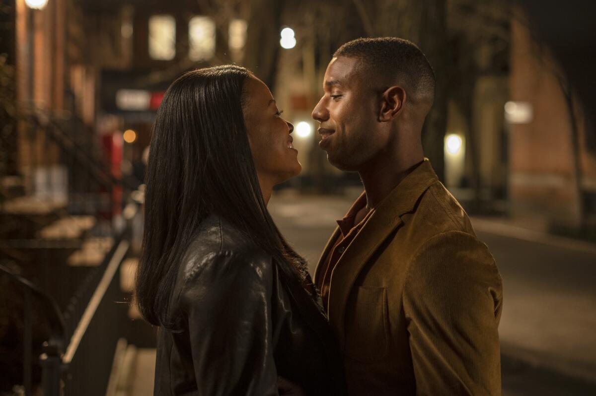 A smiling man and woman stand close together, looking at each other. 