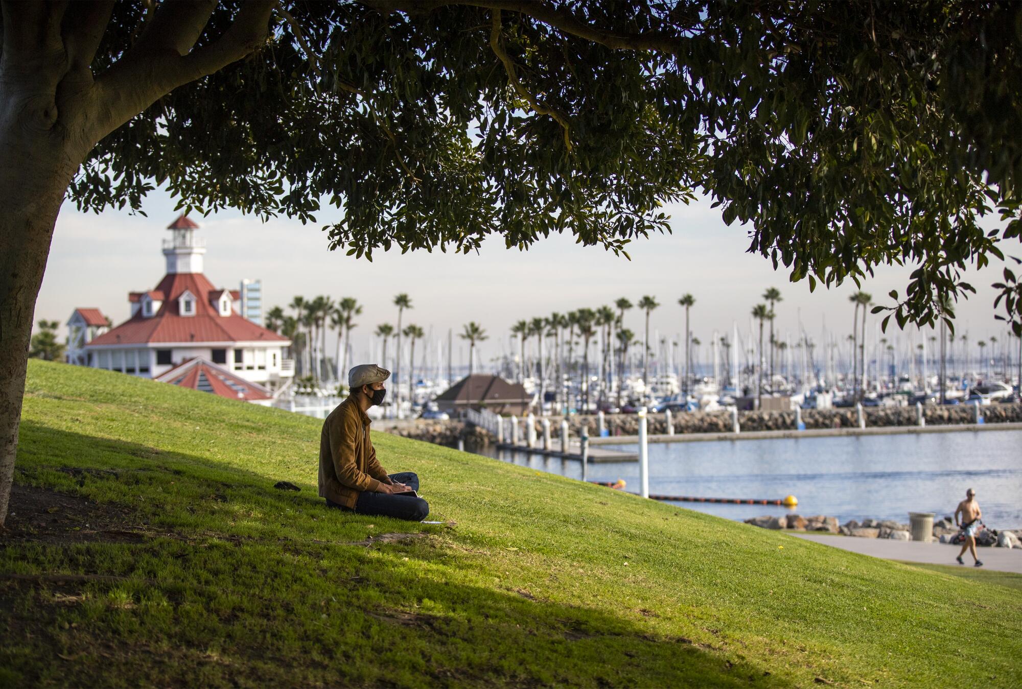 Jo Pausic pauses to look out over Long Beach Harbor while reading under a tree at ShoreLine Aquatic Park in Long Beach.