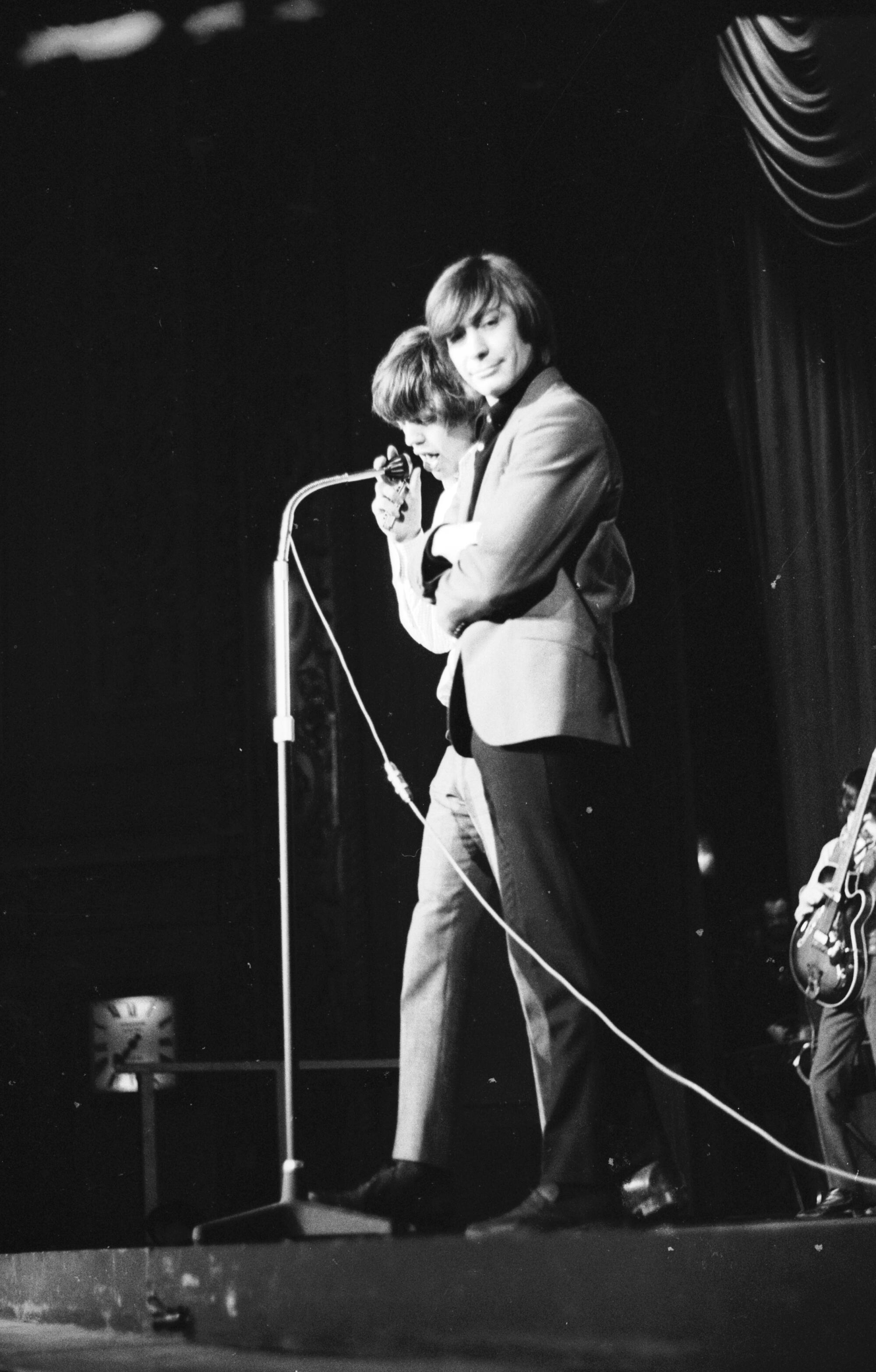 January 1965: Singer Mick Jagger and drummer Charlie Watts stand at a microphone.