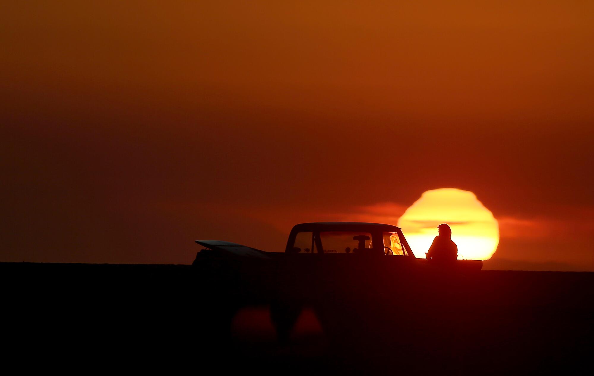 A man and his pickup truck are silhouetted by the setting sun.