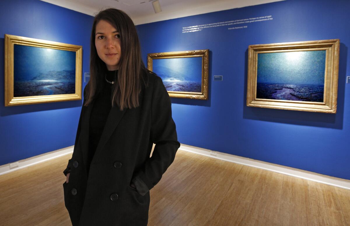 Laguna Art Museum teaching artist Ina Rosca poses in front of night scenes by painter Granville Redmond.