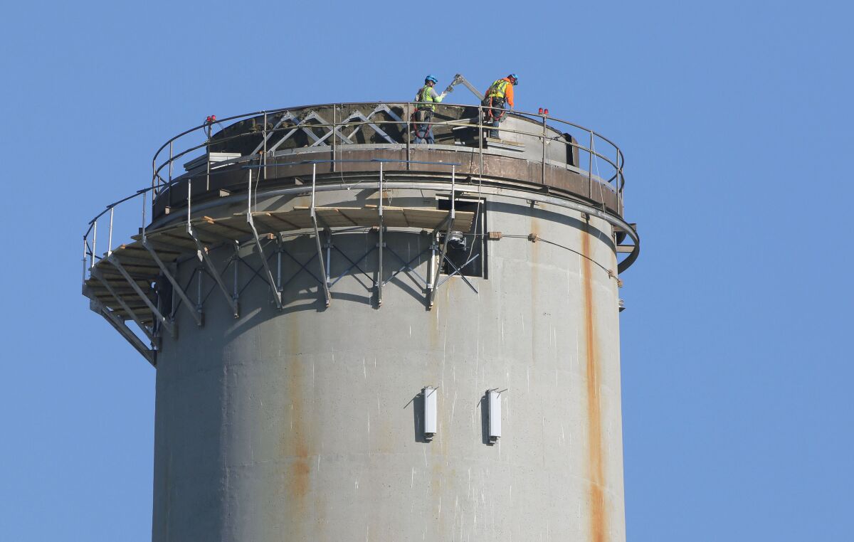 Workers on top of the Encina power plant smokestack prepare it for demolition.