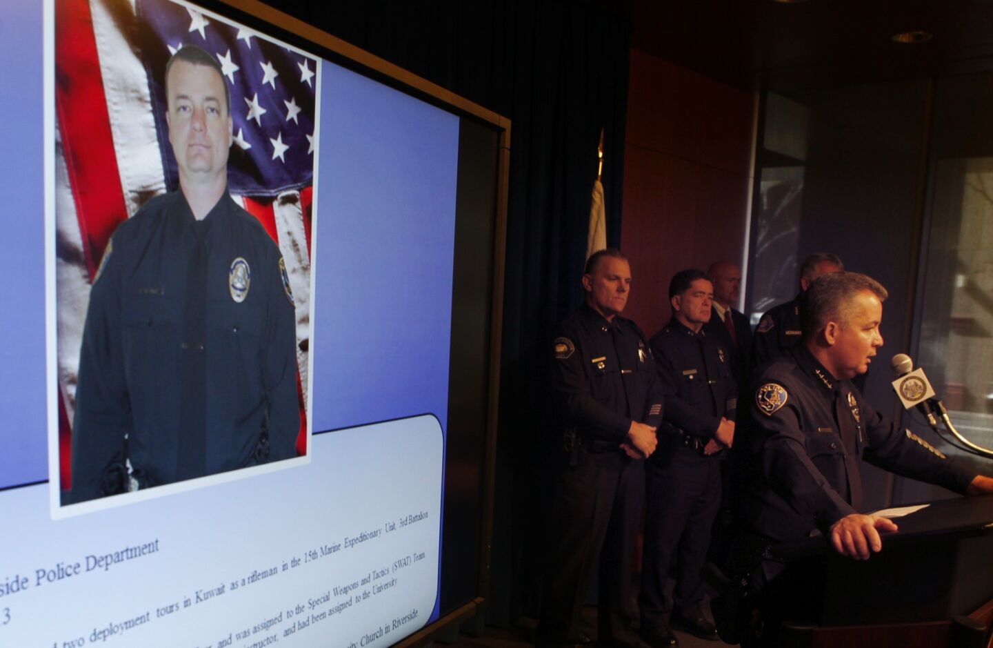 Riverside Police Chief Sergio Diaz answers questions from the media while a photo of slain Riverside Police Officer Michael Crain is projected on a screen behind him.