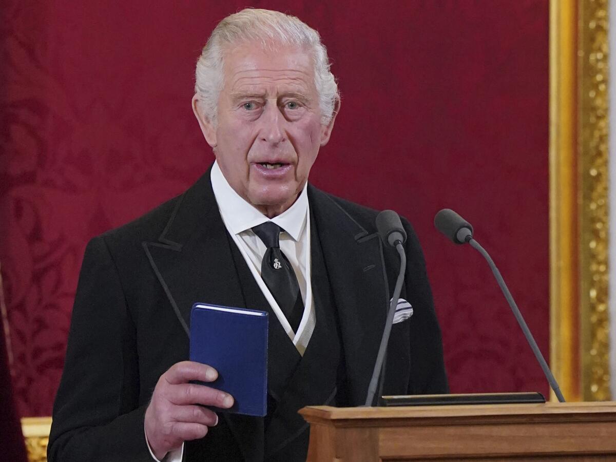 King Charles III speaks at a lectern while holding a small blue book.