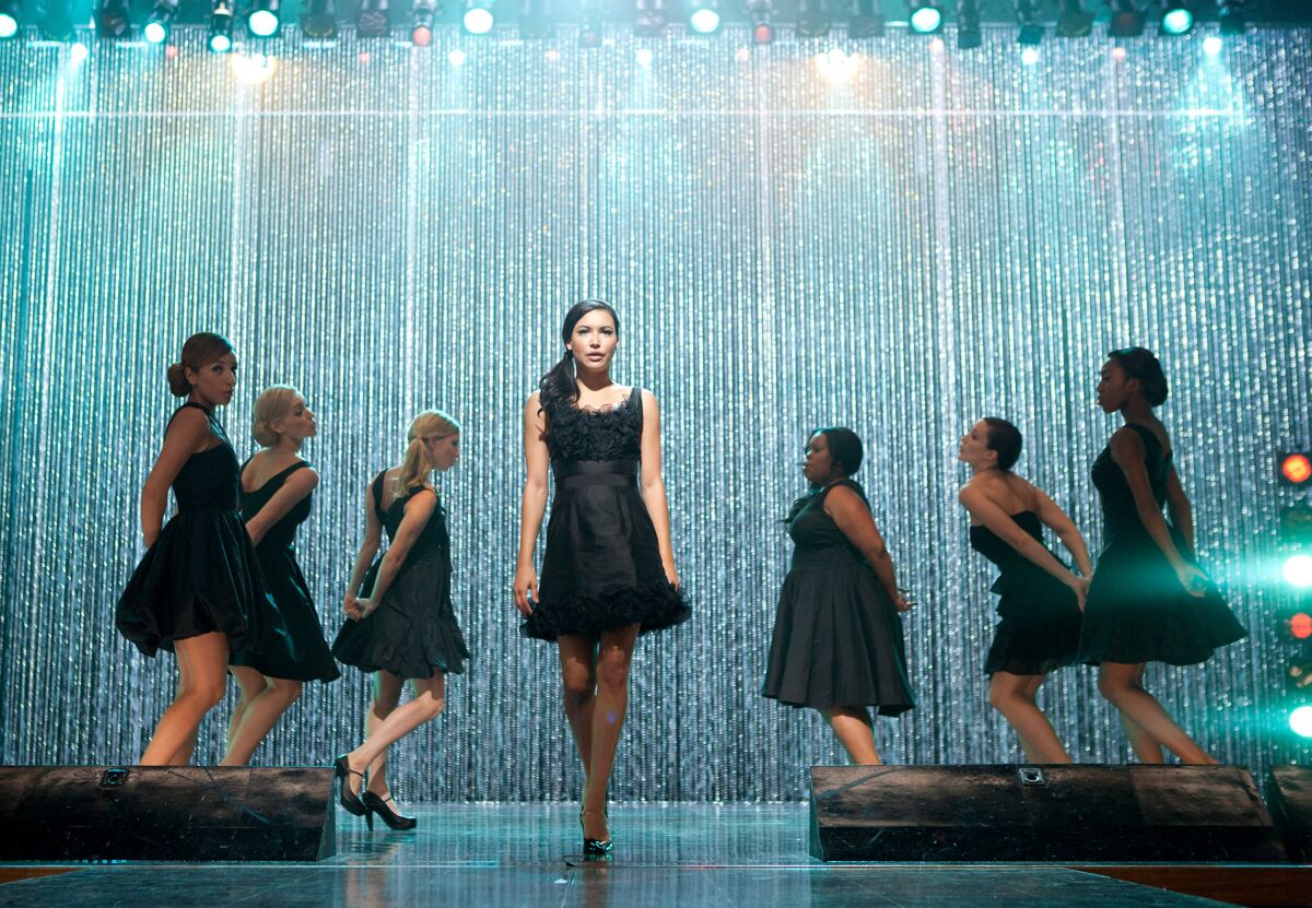 Seven women in black dresses on a stage.