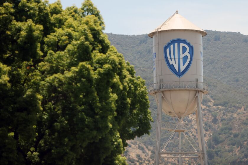 A tree next to a white water tower with the Warner Bros. logo on it 