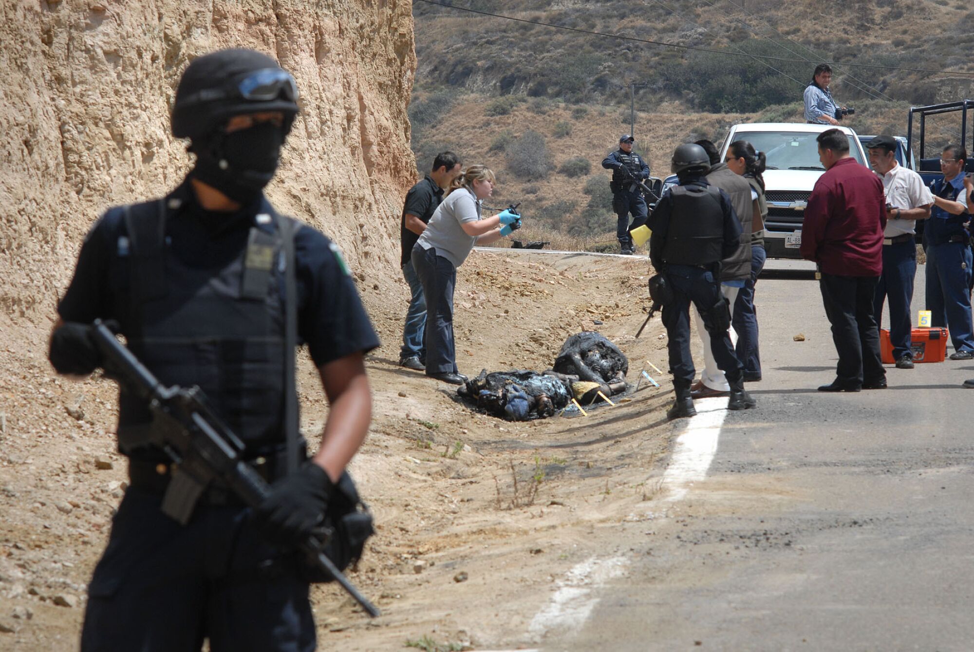 Armed officers stand guard as a forensics worker takes photos of two bodies found near the Tijuana-Rosarito Beach toll road.