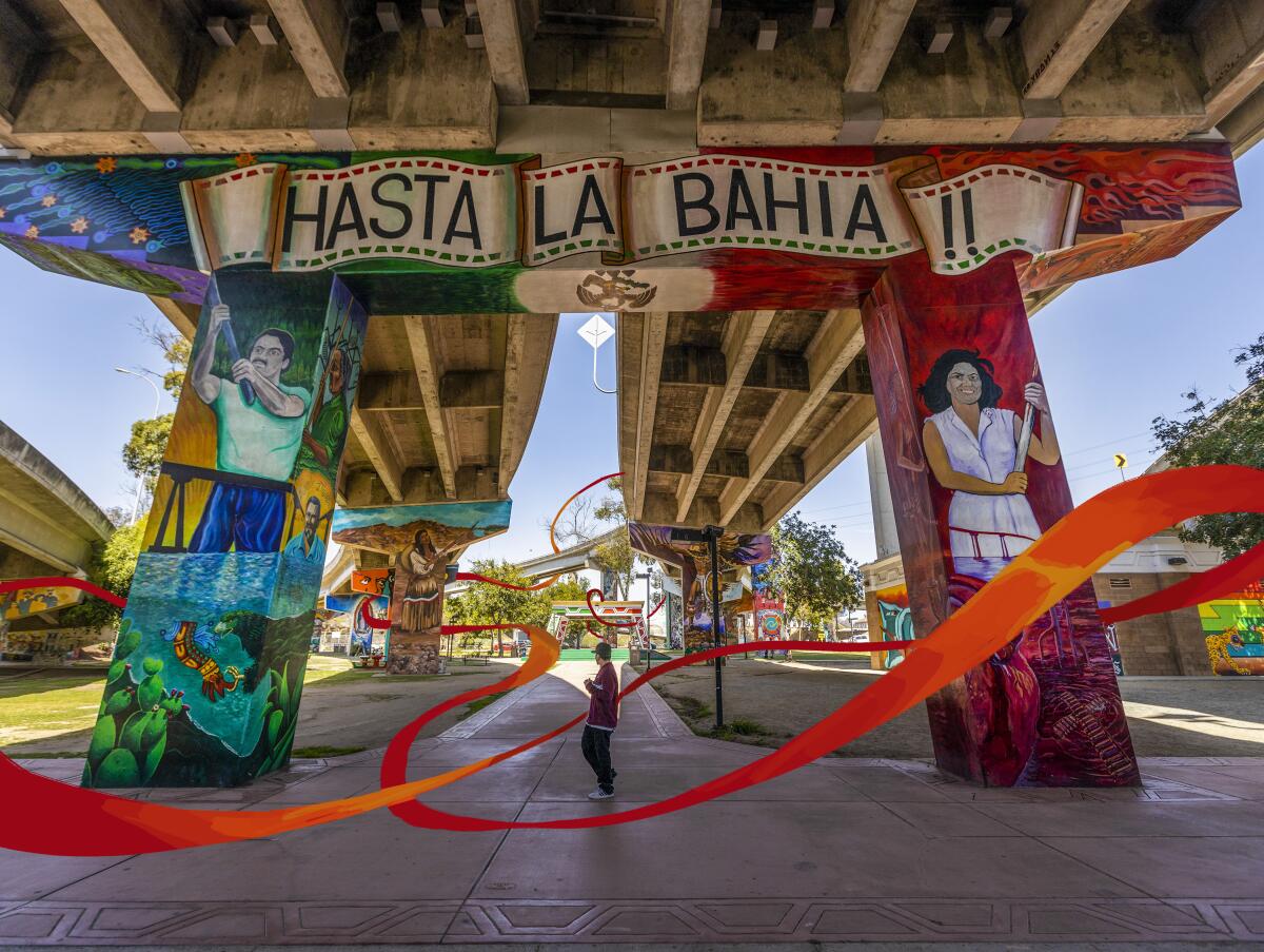 A person stands among murals painted on the supports of a concrete bridge. One says "Hasta la Bahia!" 