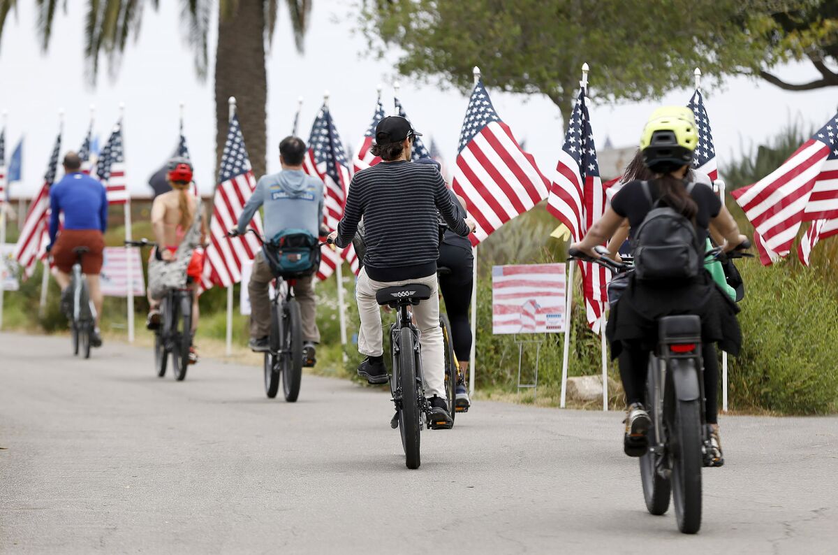 A group of bike riders pedal between rows of American flags at Castaways Park in Newport Beach.