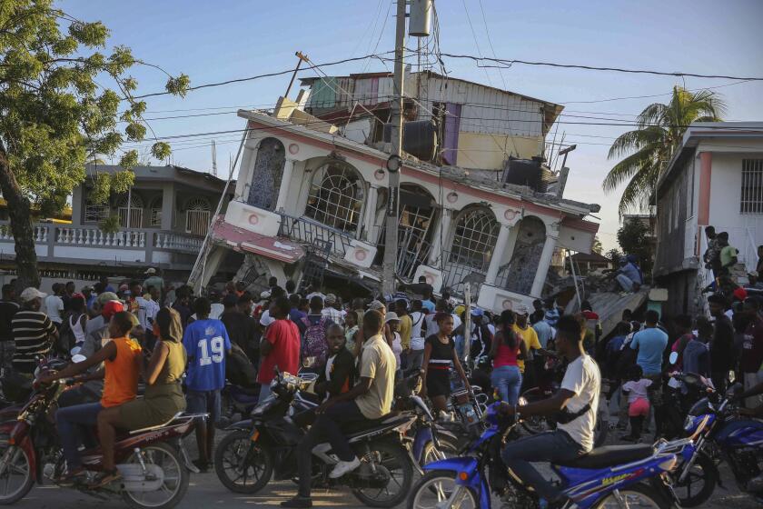 People gather outside the Petit Pas Hotel, destroyed by the earthquake in Les Cayes, Haiti, Saturday, Aug. 14, 2021. A 7.2 magnitude earthquake struck Haiti on Saturday, with the epicenter about 125 kilometers (78 miles) west of the capital of Port-au-Prince, the US Geological Survey said. (AP Photo/Joseph Odelyn)