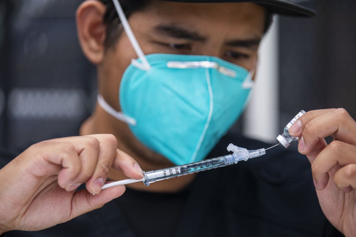 A masked worker fills a syringe with COVID-19 vaccine