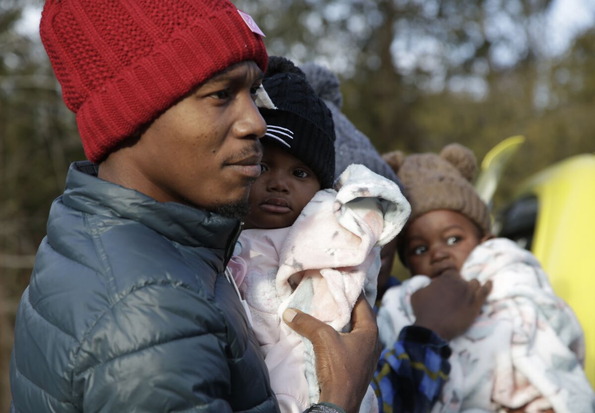 El migrante haitiano Gerson Solay, con su hija Bianca en brazos, y su familia entran a Canadá por el cruce no oficial de Roxham Road al norte de Champlain, Nueva York, viernes 24 de marzo de 2023. (AP Foto/Hasan Jamali)