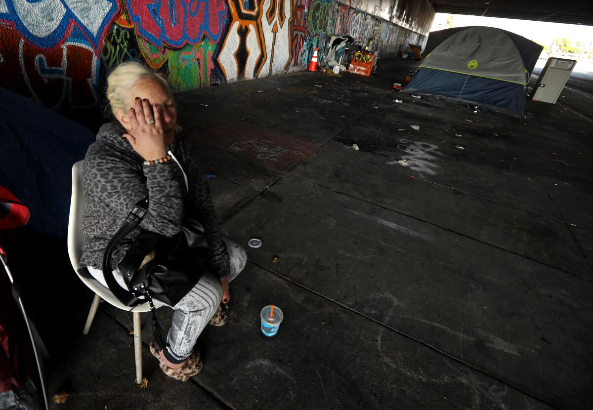 A woman wipes her face as she sits in a chair outside in an area of concrete and graffiti.