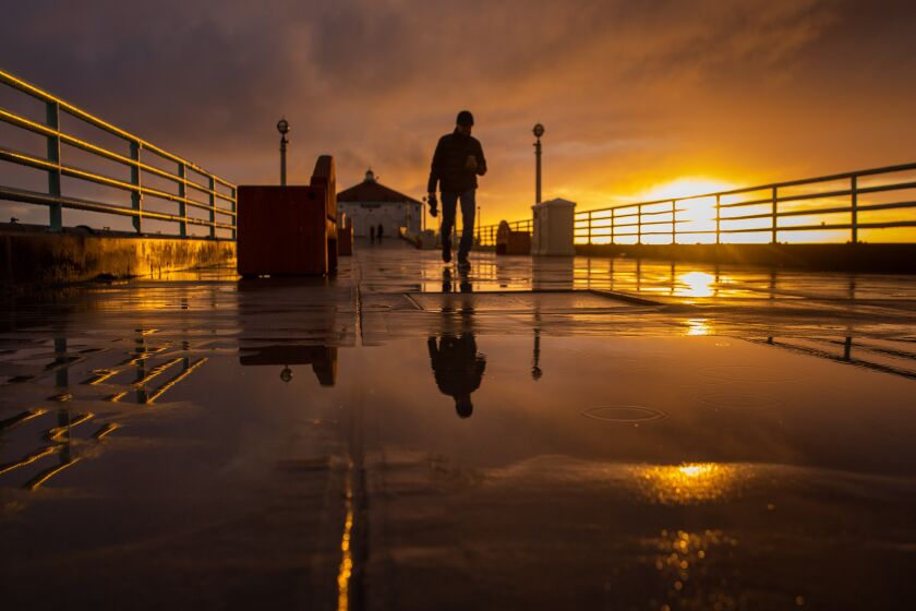 Manhattan Beach, CA - March 21: After a full day of rain, people walk on the Manhattan Beach Pier as the setting sun breaks through clouds, in Manhattan Beach, CA, Tuesday, March 21, 2023. Southern California saw another series of storms Tuesday and Wednesday. (Jay L. Clendenin / Los Angeles Times)