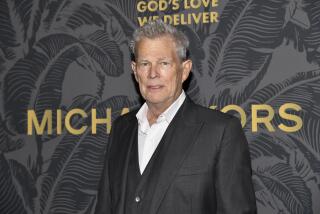 David Foster in a suit with no tie standing behind a dark background