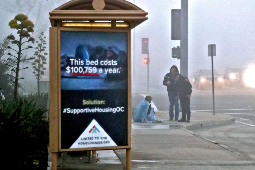 With a bus bench sign advertising supportive housing OC to end homelessness in the foreground, Costa Mesa Police senior code enforcement officer Mike Brumbaugh, right, and Costa Mesa neighborhood improvement manager Stacy Lumley, center, make contact with a homeless man sleeping on the sidewalk at Victoria and Harbor Blvd., in Costa Mesa on Tuesday, Feb. 26, 2019. The team offers assistance the area homeless.
