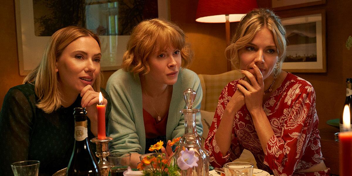 Three adult sisters huddle together at a dinner table.