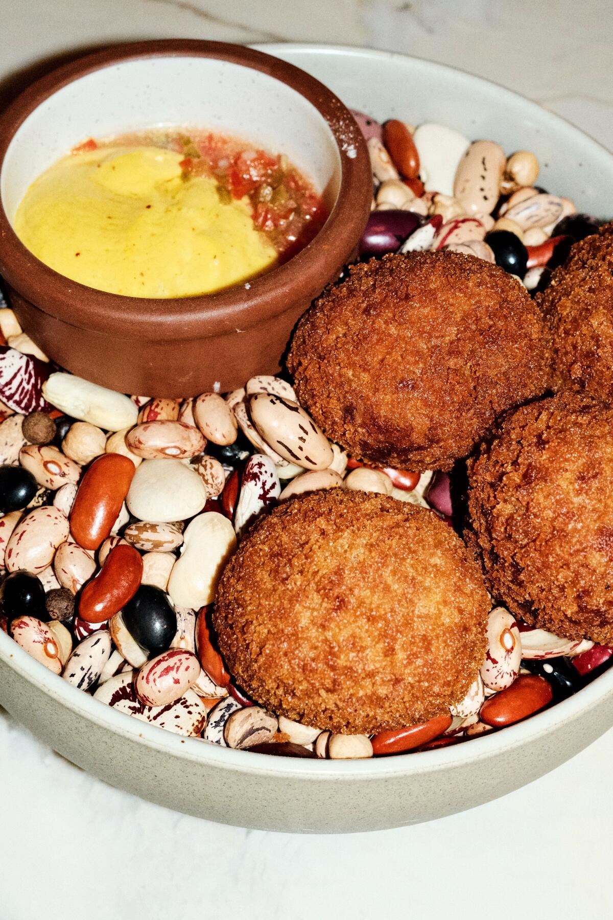 Four round saltfish croquettes in a bowl atop beans with a dipping bowl of huancaina and salsa criolla at Lucia.